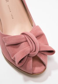 Gros plan d'une chaussure peep-toe en daim rose avec un grand nœud décoratif sur le dessus avant.