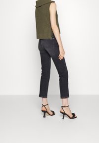 Haut tricot sans manches de couleur vert olive avec un col montant, assorti à un jean noir court et des sandales à talons noires avec un détail noué.