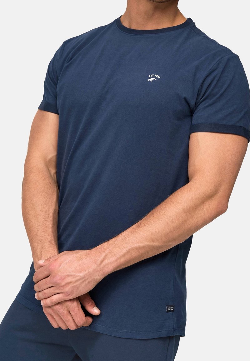 T-shirt en coton bleu marine à manches courtes, encolure ronde, avec un logo blanc sur la poitrine. Présente un col contrastant et une étiquette latérale.