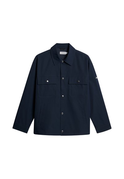 Giacca a maniche lunghe di colore blu navy scuro con colletto, chiusura frontale con bottoni, due tasche sul petto con bottone e tasche laterali, mostrata distesa su sfondo bianco.