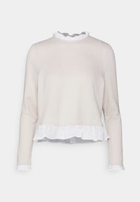 Langärmliges Oberteil in hellem Beige mit einem weißen Volantsaum und Kragen. Weicher Stoff, lockere Passform und Tupfendruck auf der Unterlage.