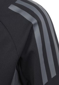 Schwarze Sportjacke aus glattem schwarzem Stoff mit grauen geometrischen Streifen auf den Schultern, die das schlanke Design betonen.