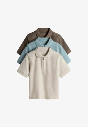 Drie polo's met korte mouwen, kraag en rits aan de voorkant, gestapeld in beige, lichtblauw en bruin op een witte achtergrond.