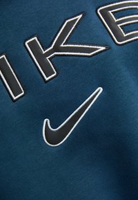 Kék szövet, amelyen feltűnő "NIKE" felirat fehér és fekete körvonalakkal, mellett egy jellegzetes fekete Nike pipa logó.