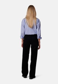 Blauwe langarmshirt met opgerolde mouwen, gecombineerd met donkere corduroybroek, met een rechte pijp en achterzakken.