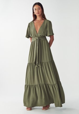 Olive green maxi dress with a deep V-neck, short puff sleeves, tie waist, and tiered skirt design, made from lightweight textured fabric.