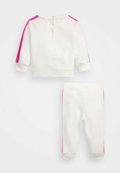 Bela trenirka in hlače z rožnatimi stranskimi trakovi. Trenirka ima tri gumbe zadaj in rebraste manšete, kar nudi udoben fit.
