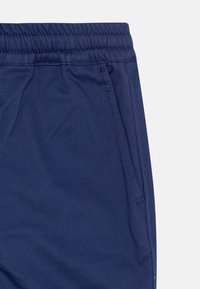 Pantalons de survêtement bleu marine avec une taille élastique, poches latérales et texture de tissu lisse. Présente des coutures surpiquées et un design décontracté.