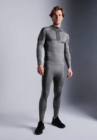 Siv outfit za športne aktivnosti z dolgimi rokavi in hlačami, ki vključuje teksturirane poudarke, pol-zadrgo na vratu in prilegajoč dizajn. Priložena črna obutev.