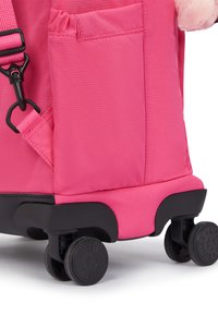 Rosa Rucksack mit strukturierter Stoffoberfläche, schwarzem Kunststoffboden und vier kleinen schwarzen Rollen. Verfügt über eine Seitentasche und einen verstellbaren Gurt.