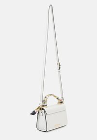 Valkoinen nahkainen käsilaukku, jossa on muotoiltu rakenne, kukkakuvioinen kahvan suojus, säädettävä olkahihna, kullanväriset metalliosat ja mustat korostejäljet.