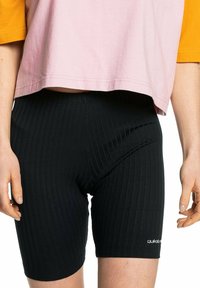 Černé žebrované šortky s elastickým pasem, na dolní straně s malým bílým logem. Textura látky vypadá elasticky a těsně.