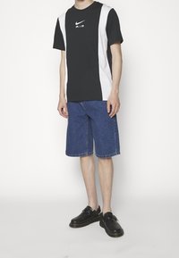 Schwarz-weiß colorblocked T-Shirt mit "AIR"-Logo, kombiniert mit blauen Jeansshorts. Schwarze Schuhe mit Schnallendetails.