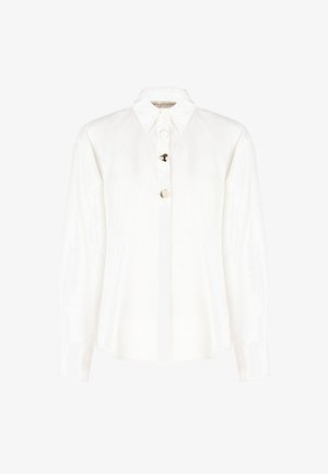 Camicia bianca con colletto, caratterizzata da una fila di bottoni circolari sul davanti. Realizzata in tessuto leggero con maniche lunghe.