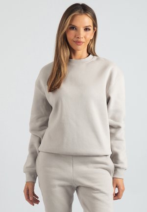 Jasnoszara bluza wykonana z miękkiego, fakturowanego materiału. Posiada okrągły dekolt, długie rękawy i luźny krój. W zestawie z pasującymi spodenkami dresowymi.