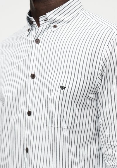 Camisa branca com botões, com finas riscas azuis-escuras, gola clássica, botões castanhos e um pequeno logótipo no bolso do peito.