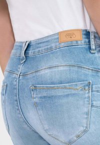 Lichtblauwe spijkerbroek van denim met een licht vervaagde textuur, voorzien van een bruine leren label en dubbele gestikte zakken op de achterkant.