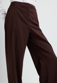 Bruine, gestreepte broek met een getailleerde pasvorm, vervaardigd uit gladde stof. Heeft een hoge taille en een wijde broekspijpvorm voor een gestructureerde uitstraling.