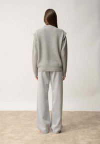 Maglione grigio a coste con spalle ampie, abbinato a pantaloni larghi grigi chiari. Tessuto morbido, tonalità neutre, design minimalista.