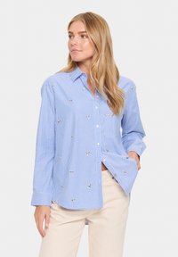 Camisa abotonada de rayas azul claro y blanca con palmeras bordadas decorativas, mangas largas y un corte relajado.