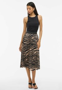 Top senza maniche nero abbinato a una gonna midi plissettata con un motivo a strisce zebra beige e nero, completato da sandali neri.