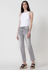 Fehér ujjatlan body, világosszürke slim fit farmernadrág és fekete platform szandál. Sima anyag, testhezálló fazon és enyhén kopott textúra a farmernadrágon.