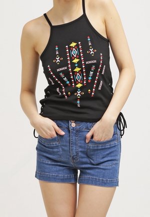 Top negro tipo halter con bordados geométricos coloridos, combinado con shorts de mezclilla que cuentan con bolsillos delanteros y dobladillo vuelto.