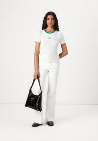 Camiseta corta de color gris con cuello verde y el logo de 'GAP', combinada con pantalones blancos acampanados y un bolso de cuero negro. Bailarinas negras.