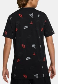 T-shirt di cotone nero con un motivo di vari loghi e frasi Nike in rosso e bianco, maniche corte e scollo rotondo.