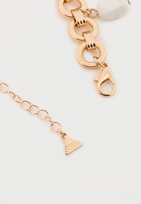 Guldfarvet kædearmbånd med sammenkoblede cirkler, en krabbe-lås og en trekantet charm med textured striber.