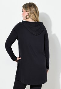 Zwarte hoodie met lange mouwen en een ontspannen pasvorm, met een gladde textuur en een gebogen zoom, gecombineerd met donkere spijkerbroeken.