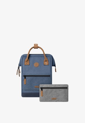 Zaino in tessuto blu con dettagli in pelle marrone, dotato di una tasca frontale con zip e di un manico. Include una piccola pochette grigia con zip sotto.