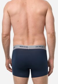 Marineblaue Boxershorts mit einem grauen elastischen Bund, der die Aufschrift "denim brøs" und "est.89 cal" trägt. Glatte Textur, enganliegendes Design.