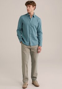 Világoskék, hosszú ujjú ing len anyagból, gombos kialakítással, világosszürke nadrággal és bézs cipővel párosítva. Egyszerű, minimalista részletezés.