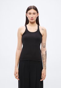 Μαύρο ριμπ καλοκαιρινό τοπ με στρογγυλή λαιμόκοψη και λεπτές τιράντες, σε συνδυασμό με άνετο μαύρο παντελόνι. Διαθέτει διακριτική λεπτομέρεια με το λογότυπο της μάρκας στο μπροστινό μέρος.