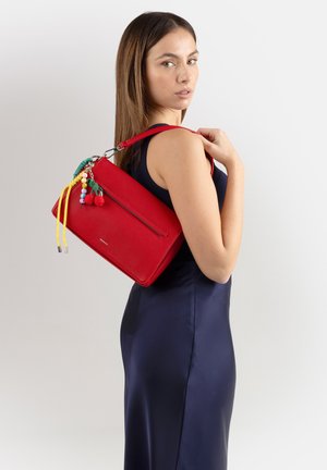 Donna con un vestito senza maniche blu navy che porta una borsa rossa con nappe colorate di perline sulla spalla, guardando oltre la schiena.