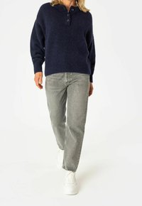 Maglione blu navy in misto lana con scollo henley con bottoni, abbinato a jeans grigio chiaro a gamba dritta e sneakers bianche.