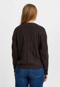 Mörkbrun stickad tröja med ett strukturerat mönster, ribbad nederkant och långa ärmar, tillsammans med blå jeans. Har en avslappnad passform.