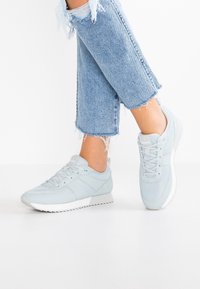Chaussures de sport bleu clair en mesh et matériaux synthétiques. Caractérisées par une tige texturée, une semelle blanche et des détails de marque subtils.
