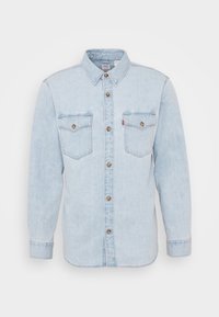 Chemise en denim bleu clair à manches longues, boutonnée sur le devant, col pointu et deux poches poitrine avec boutons et détails de couture.