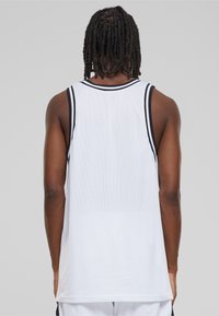 Hvit mesh basketball tank topp med svart kant, uten ermer og løs passform. Strukturet stoff og lengre bakhem.