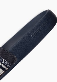 Tongs marines avec une sangle en caoutchouc texturé portant un détail en relief "SUPERDRY", et un tissu tissé contrastant au design à motifs.
