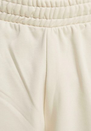 Light beige sweatpants featuring a gathered waistband, soft cotton fabric, smooth texture, and pleats near the pockets for added detail.