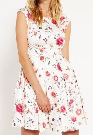 Witte mouwloze jurk met aansluitend lijfje en uitlopende rok, met een kleurrijk bloemen- en vogelpatroon.