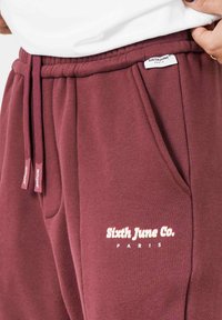 Bordeaux joggingbroek met elastische tailleband, zijzakken en witte tekst 'Sixth June Co. PARIS' op het onderbeen. Zachte textuur, casual pasvorm.