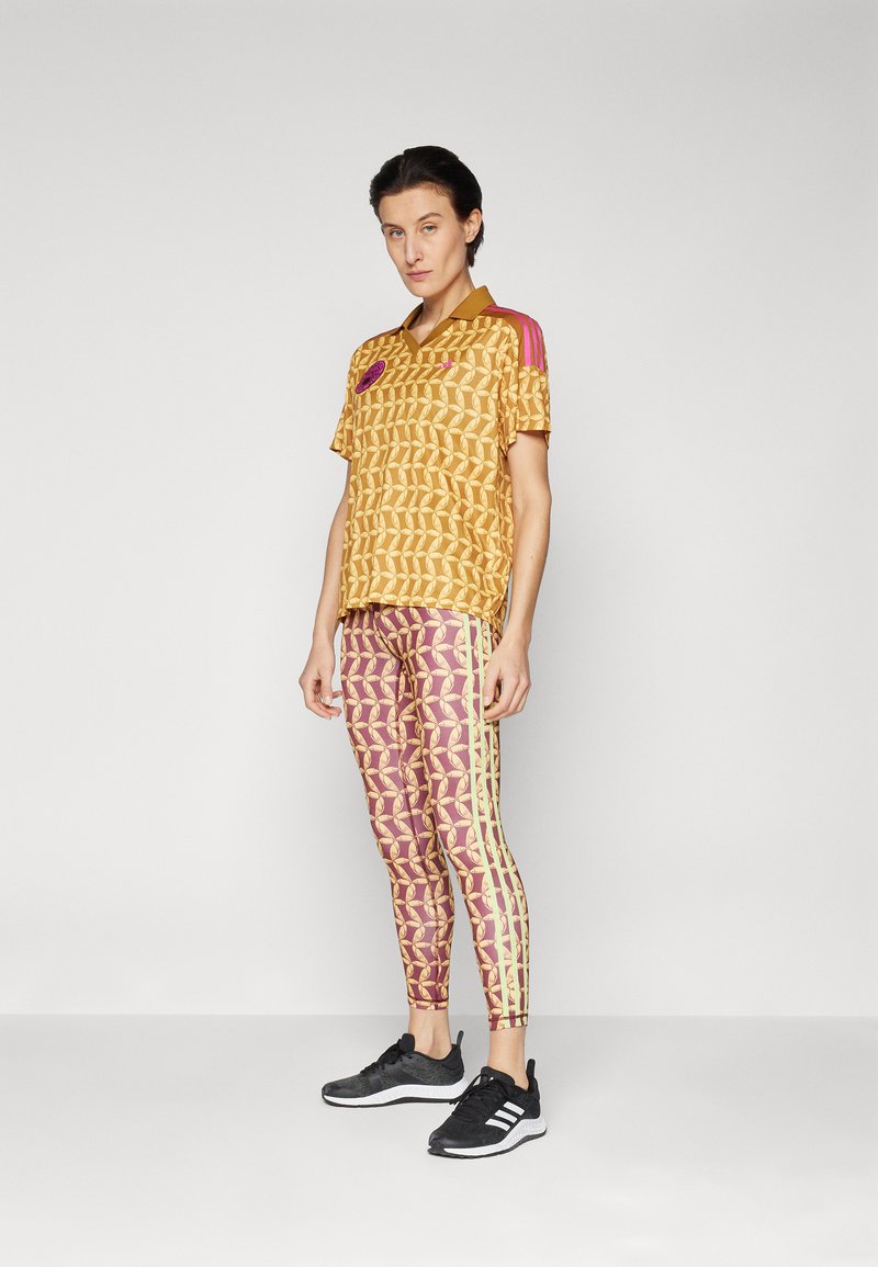 Completo sportivo composto da una maglietta a maniche corte con motivo dorato e colletto marrone, accenti rosa, abbinata a leggings rosa con strisce gialle.
