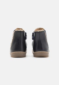 Botas de tornozelo em couro azul marinho com um acabamento texturizado, detalhe em tom cru com recortes ondulados e fechos laterais. Apresentam uma sola de borracha flexível para conforto.