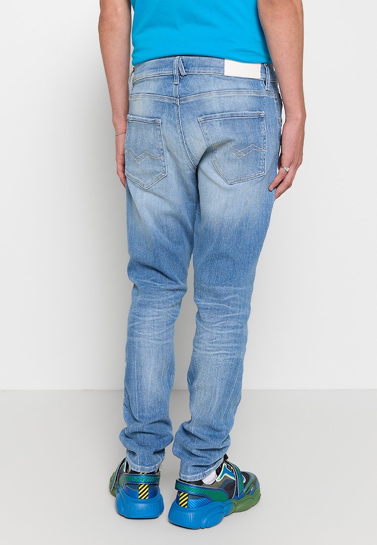 Helle blaue Jeans aus Denim mit einem verwaschenen Finish, ausgestattet mit zwei Gesäßtaschen mit genähten Akzenten, kombiniert mit bunten Sneakers.