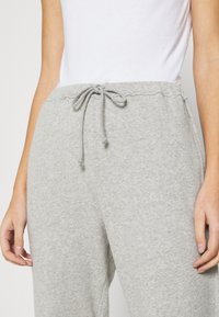 Harmaat puuvillaiset collegehousut, joissa on nauhavyötärö, pehmeä rakenne ja elastiset hihat. Mukana näkyvät saumat ja sivutaskut.