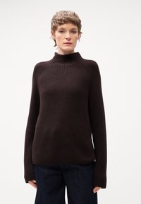 Maglione marrone a maglia con collo alto, maniche lunghe e un motivo a coste testurizzate. Abbinato a jeans scuri, che evidenziano una vestibilità comoda.